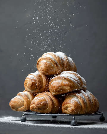 Sweet puff pastry. Pyramid of appetizing baked bagels sprinkled with powdered sugar on gray...