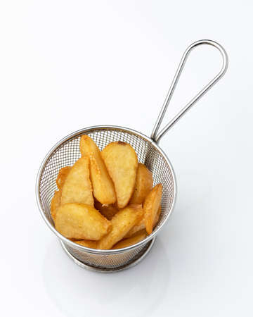 Appetizing snack. Crispy deep-fried potato slices in metal sieve or colander. Object isolated on white background. Tasty food. Kitchen utensils.の写真素材