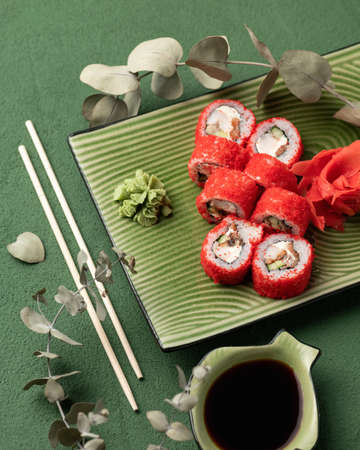 Flat lay. Red Sushi roll in masago or tobiko caviar. Inside-out Sushi Set on green background....