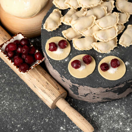 Raw Sweet Dumplings stuffed with cherry. Convenience Food. Cooking process. Slices of dough with filling and rolling pin on kitchen table. Top view. Square format. Soft focus.の写真素材