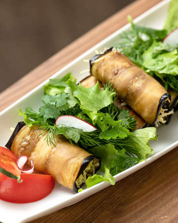 Eggplant Rolls. Vegetable appetizer with greens. Stuffed rolls of fried eggplant slices on plate with tomatoes and parsley. Vertical format. Soft focus.の写真素材