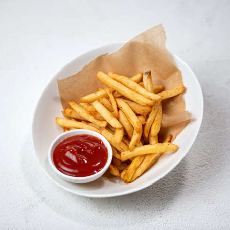 Fried potatoes with tomato sauce, fries with ketchup. Food plate isolated on white background.