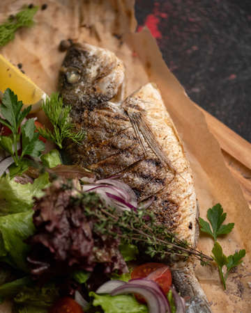 Fried whole fish with herbs and vegetables on parchment paper. Soft focus. Top view.の写真素材
