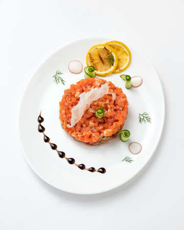 Festive salad or Snack with red sturgeon fish and vegetables. Pieces of salmon, lemon slices and cucumber rolls on white plate. Top view. Vertical format.の写真素材