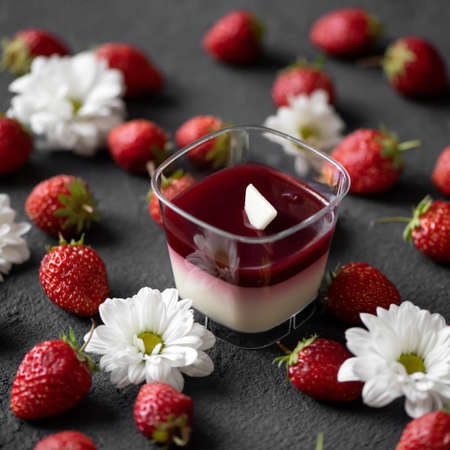 Strawberry panna cotta in glass on gray table with fresh berries and white gerbera flowers on it. Top side view. Soft focus.の写真素材