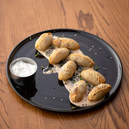 Dumplings with sour cream and herbs. Black plate of tasty food on wooden table. Soft focus. Square format.の写真素材