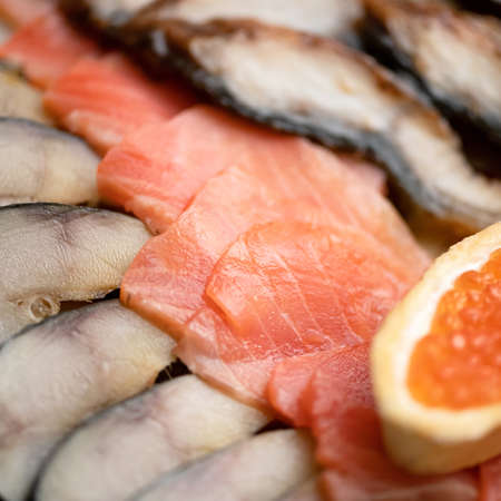 Close-up of Seafood plate. Slices of red salmon fish, pieces of mackerel and sandwich with red caviar in foreground. Soft focus.の写真素材