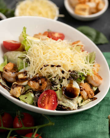 Caesar salad. Bowl of delicious snack or appetizer of chopped vegetables, grated cheese and seafood. Close-up shot. Vertical format. Soft focus.の写真素材