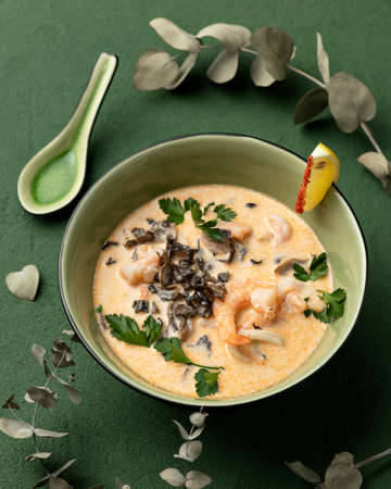 Thai soup Tom Yam with shrimps. Bowl of spicy hot food on green background. Pan-asian cuisine. Oriental meal. Vertical format.の写真素材