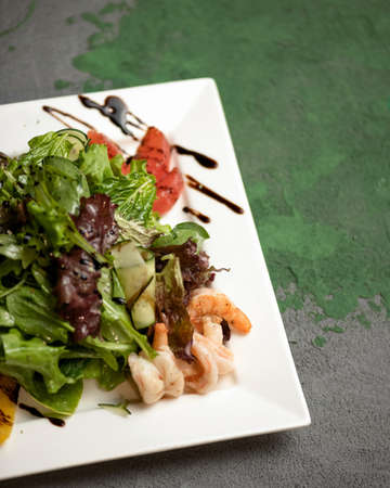 Close-up of Fresh vegetable salad with shrimps. Square Plate of healthy food and ingredients for its preparation on gray table. Vertical format. Soft focus. Copy space.の写真素材