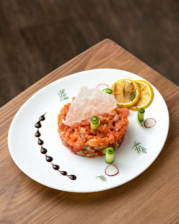 Appetizer of red sturgeon fish and vegetables. Platter with salmon pieces, lemon slices and cucumber rolls on on wooden table. Top side view. Copy space. Vertical format.の写真素材