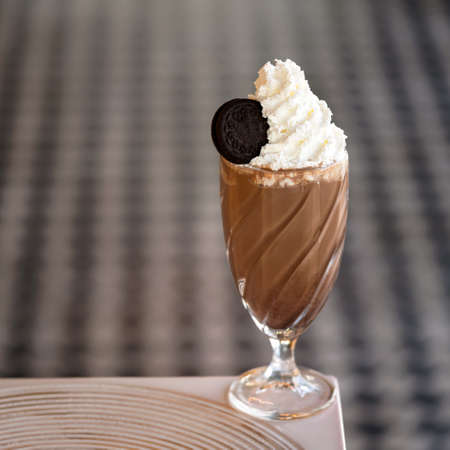 Refreshing drink. Glass of chocolate milkshake cocktail with Airy foam or froth and cookie on top. Puffy whipped cream dessert on blurred background. Soft focus. Soft focus. Copy space at left.の写真素材