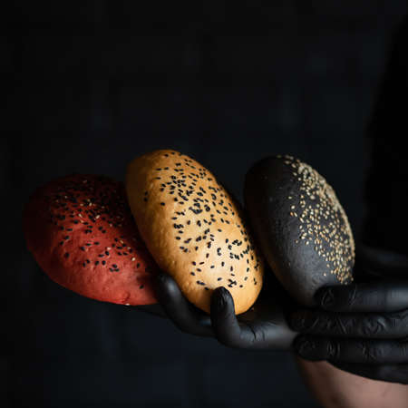 Chef holding different types of bread. Hand in black glove demonstrates red, white and rye loaf of bread with sesame seeds on black background. Close-up shot. Copy space.の写真素材