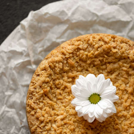 Romantic dessert. Cake or shortcrust pastry tart decorated with white gerbera flower on parchment paper. Close-up shot. Top view.の写真素材