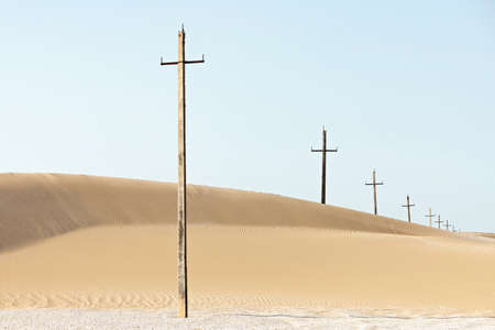 Crosses in desert. Ancient electricity power line poles in sand dune.