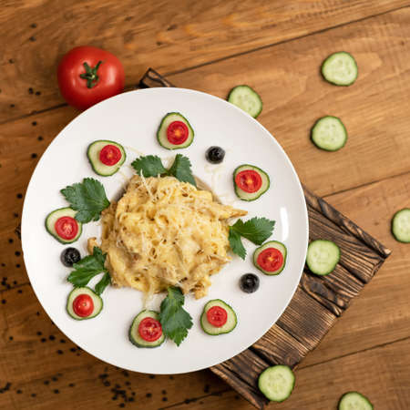 Spaghetti with melted cheese, garnished with slices of cucumber, tomato and parsley or celery. Gourmet serving plate of italian food on wooden background. Top view. Flat lay.の写真素材
