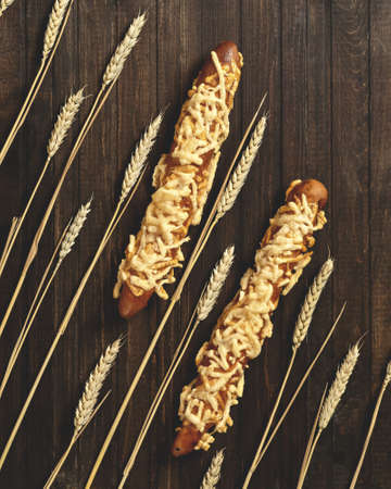 Golden cheese baguettes. Two whole loaves of crispy bread with cheese topping on dark wooden table with wheat spikelets on it. Top view. Vertical format.の写真素材