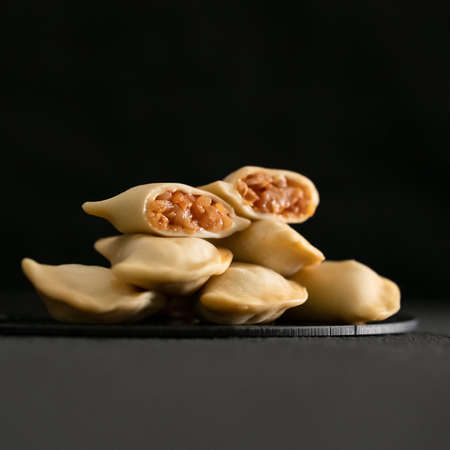 Hot boiled dumplings with stewed cabbage filling on black background. Cooked dumplings cross section. Convenience Food, dough stuffed. Close-up shot. Soft focus. Side view. Square format. Copy space.の写真素材