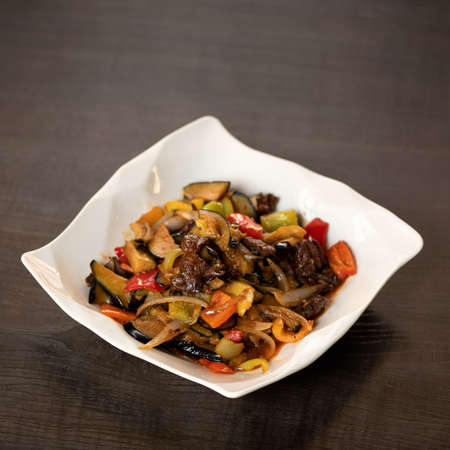 Plate with stir-fried meat and vegetables on wooden background. Oriental Cuisine. Copy space. Soft focus.の写真素材