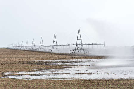 Automated Agricultural installation irrigates brown ground. Water sprinkler, farming irrigation system. Field aerator machine in action.の写真素材