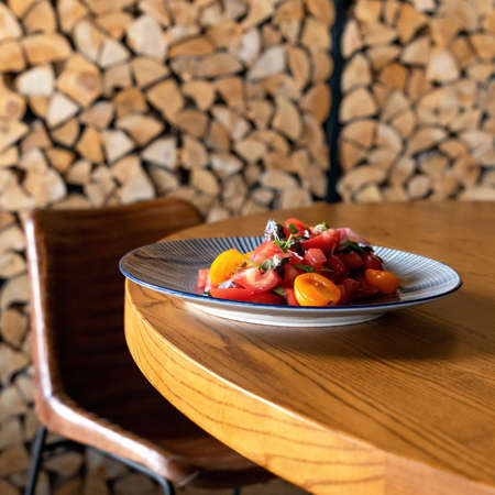 Plate of fresh tomatoes salad on restaurant wooden table. Blurred background. Soft focus. Copy space.の写真素材