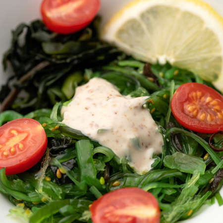 Close-up of seaweed salad with cherry tomatoes and lemon with spicy sauce. Healthy eating. Soft focus. Square format.の写真素材