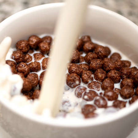 Crispy chocolate balls with milk pouring in bowl. Delicious breakfast. Dairy and cereal products. Close-up shot. Soft focus.の写真素材