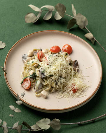 Noodles with tomatoes, mushrooms and grated Parmesan cheese. Platter of Asian food on green background. Pan-Asian cuisine. Soft focus. Vertical format.の写真素材