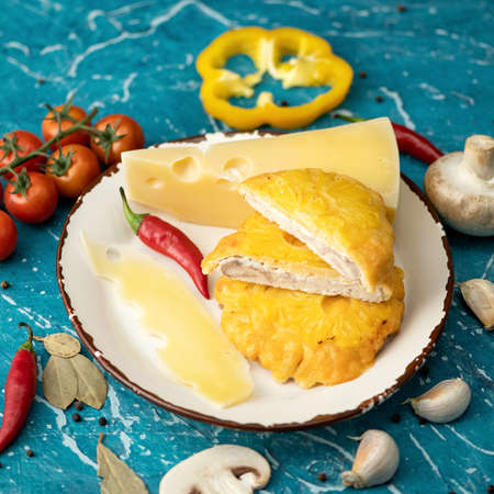 French poultry meat with cheese and pineapple. Plate with Baked or Fried chicken fillet with vegetables on blue table. Close-up shot. Soft focus.の写真素材