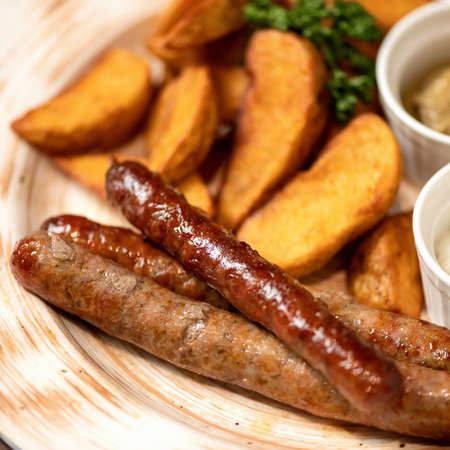 Close-up of fried sausages and potatoes with mayonnaise and mustard on clay plate. Simple rustic lunch. Junk food concept. Soft focus.の写真素材