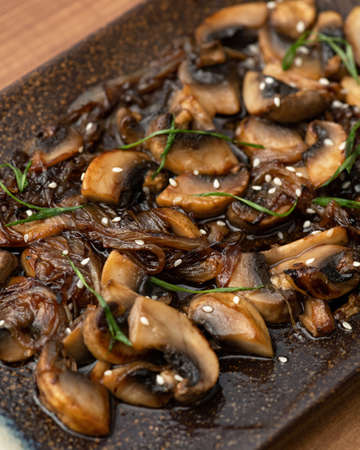 Fried mushroom slices on platter. Close-up shot of Clay plate with cooked champignons, herbs and sesame seeds. Soft focus.の写真素材