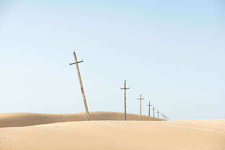 Crosses line in sand desert. Christian symbol of faith and hope. Old cross-shaped pillars on sky background. Ancient Power electrical transmission. Copy space.の写真素材