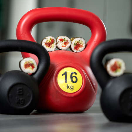 Sushi rolls and weights for strength training. Wellness and japanese food, power for muscles. Close up shot. Soft focus.の写真素材