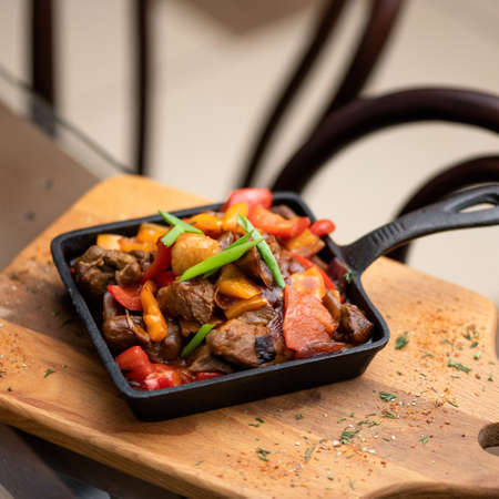 Stewed meat and vegetables in cast iron pan. Healthy rustic food on wooden cutting board. Soft focus.の写真素材