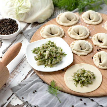 Raw dumplings, dough stuffed with cabbage and dill on wooden table. Vegetarian convenience food. Cooking Process.の写真素材