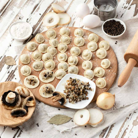 Making process of Dumplings with mushrooms and onion filling. Raw dough and Ingredients to making convenience food on rustik table. Top side view. Soft focus.の写真素材
