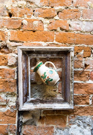 Jug in old picture frame hangs on old brick wallの写真素材