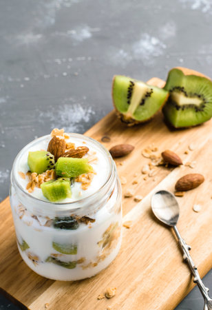 Yogurt parfait with kiwi, granola and almond nuts. Healthy organic breakfast concept. Served with decorative spoon on wooden board.の写真素材