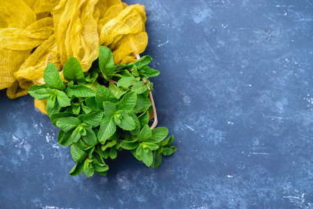 Green fresh organic mint in small wooden basket. On concrete dark table background with gauze table...