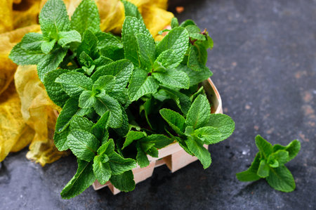 Green fresh organic mint in small wooden basket. On concrete dark table background with gauze table...