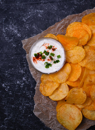 Potato chips with dip on parchment paper. Dark concrete background. Top viewの写真素材