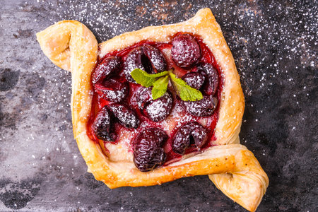 Homemade puff pastry with cherry. Sweet tasty dessert. Decorated with mint leaves. On old black cooking sheet.の写真素材