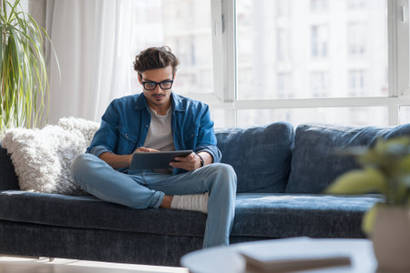 Casual remote work lifestyle in living room with tablet on sofa, cozy modern interior and daylight.の素材