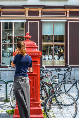young woman posting letters in red mailbox outdorの写真素材