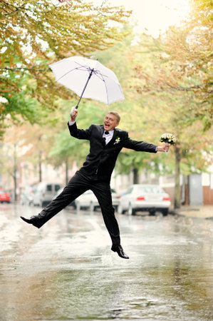 Bridegroom jumping with white umbrellaの写真素材