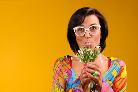 Pretty girl in glasses and snowdrops in the hands over yellow backgroundの写真素材