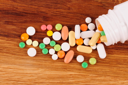 Stack of different pills  near the opened container on wooden deskの写真素材