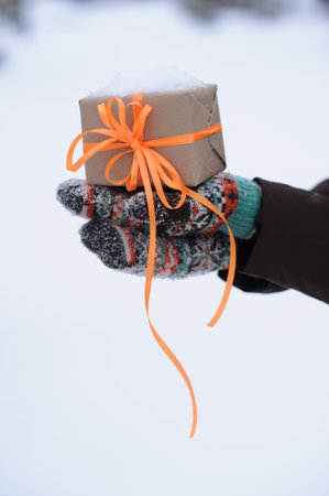 gift with orange stripes in hands in winterの写真素材