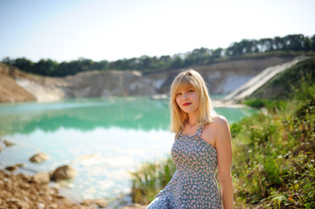 Dreaming girl sitting on bridge with forest and river on the background. Lonely sad woman by the lake. Beautiful woman in elegant vintage blouse, skirt, floppy hat. Natural sensual woman outdoorsの写真素材