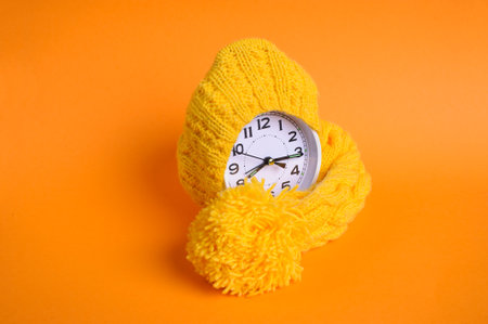 Alarm clock in yellow hat on the orange backgroundの写真素材